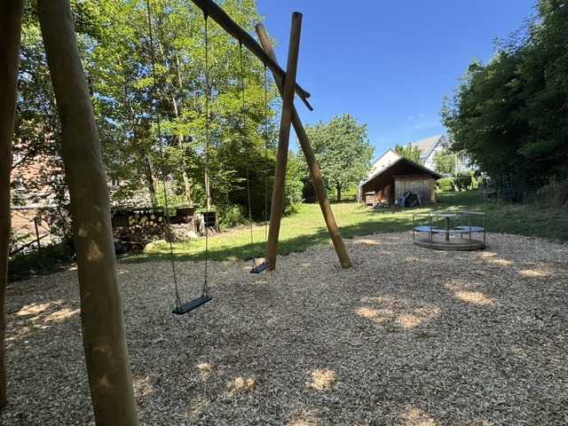 neuer Spielplatz der Naturfreunde Degerloch: links eine große Schaukel, weiter hinten rechts ein Karussell und im Hintergrund der Schuppen